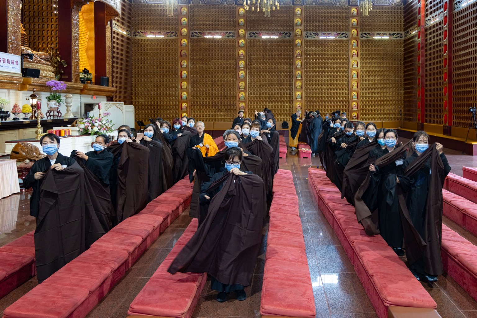 Group etiquette training, with guiding monastics instructing preceptees on wearing the chanting rode and precepts robes.