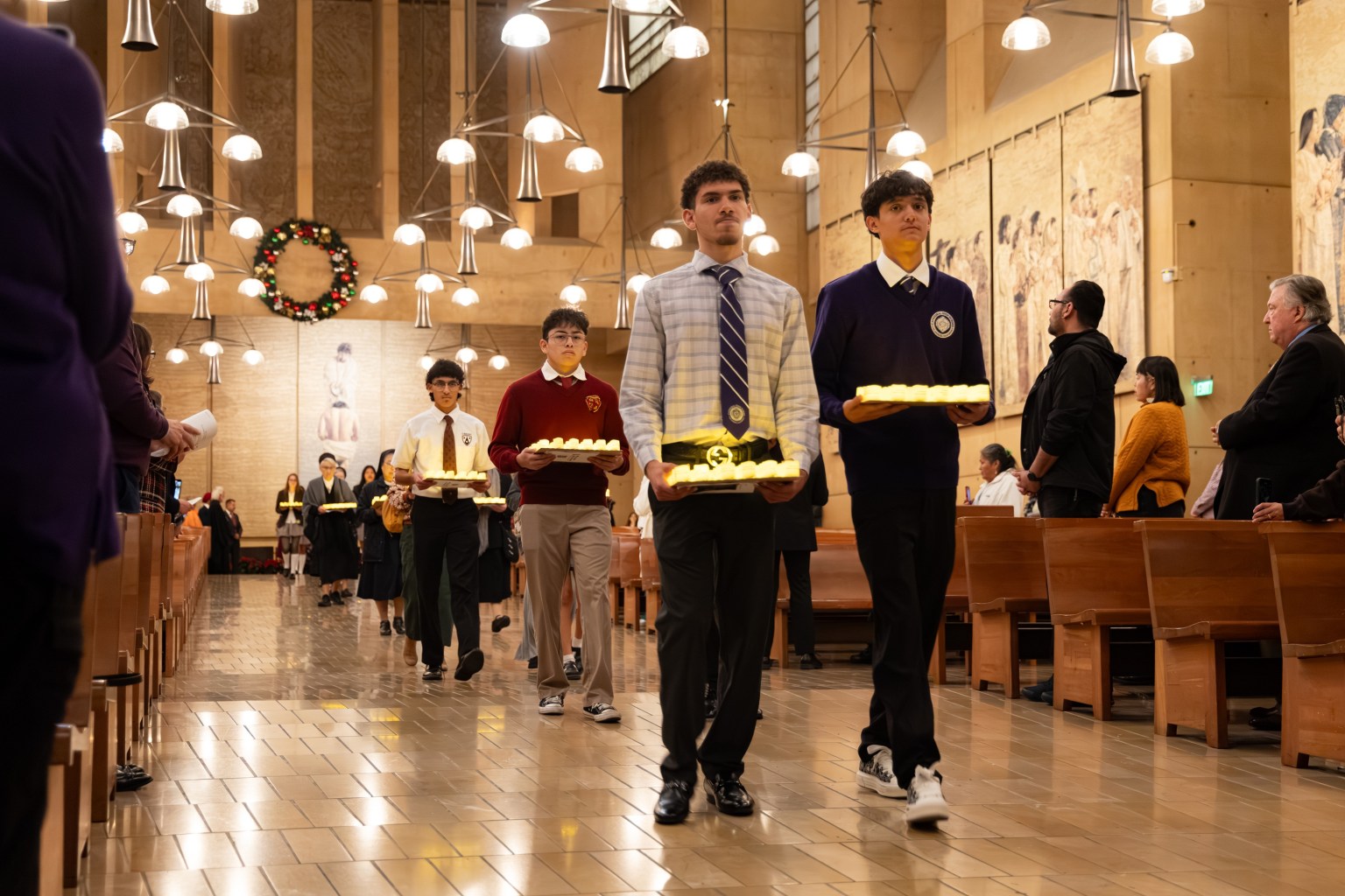 Students from Catholic and non-Catholic schools hold candles bearing the names of unhoused individuals who have passed away, slowly processing into the cathedral—symbolizing shared responsibility for hope across generations and among faiths.