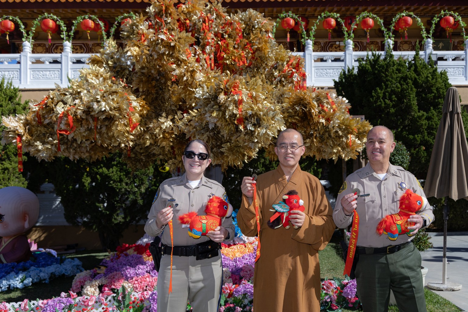 Venerable Huidong (center), Chief Glenn Emery (right), and Commander Melissa Hammond (left) pose for a photo in front of the Wishing Tree.